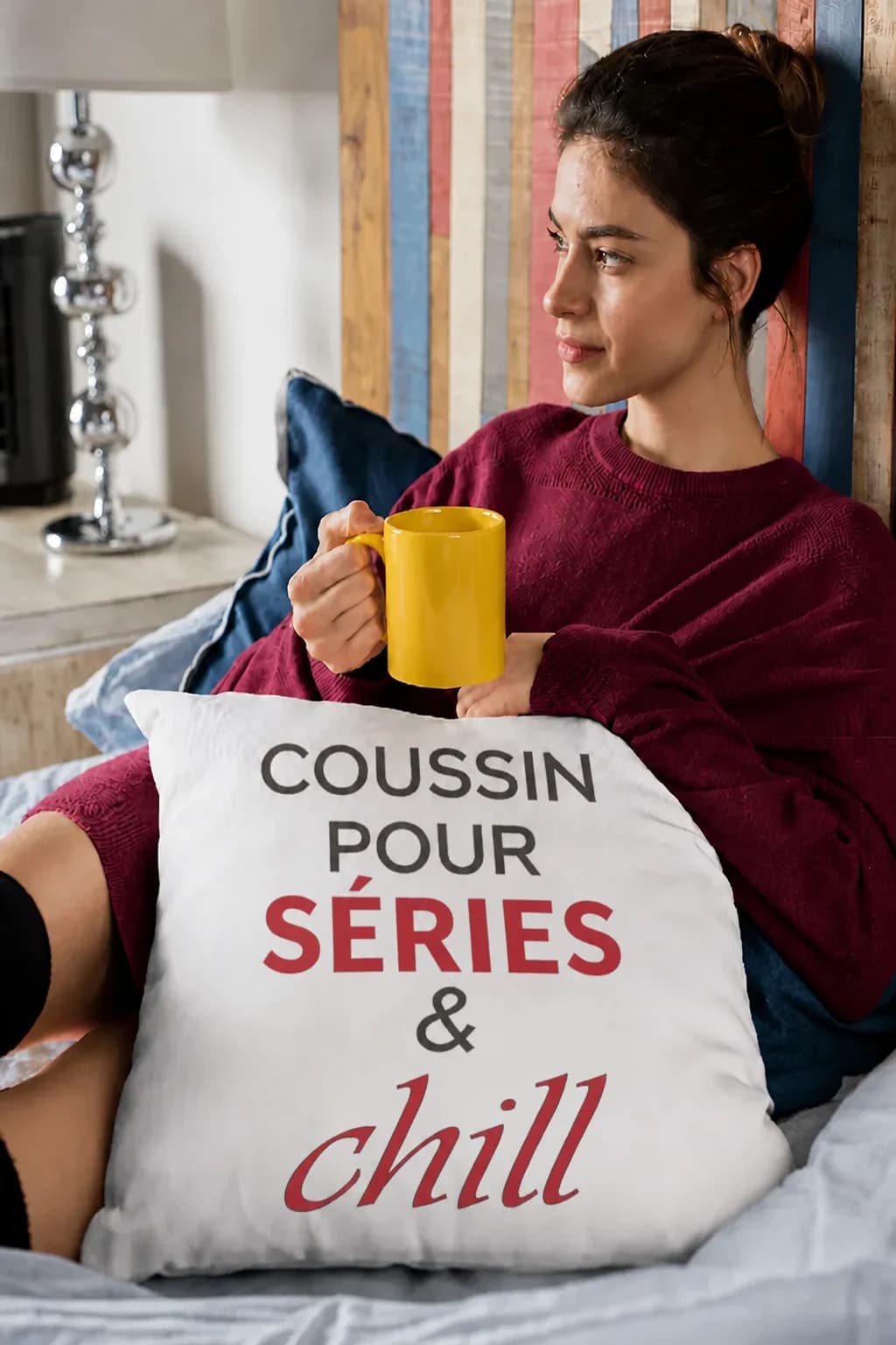 Jeune femme avec un mug sur son lit, appuyée sur un coussin blanc « Coussin pour séries & chill »