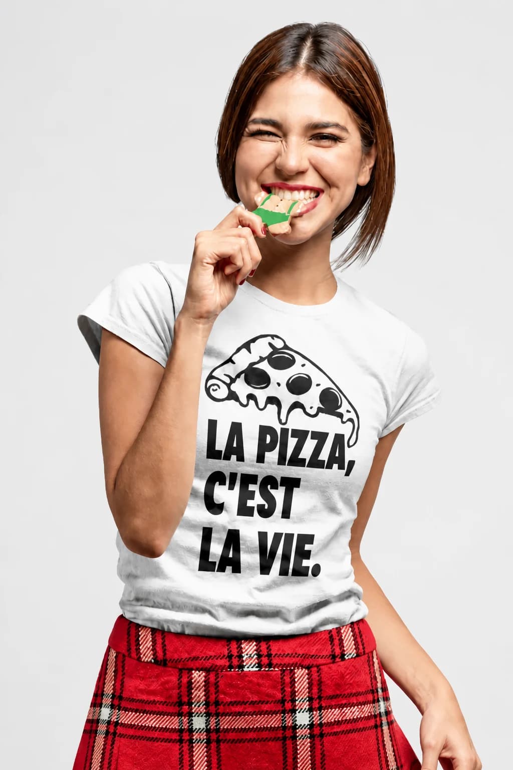 Jeune femme croquant une part de pizza, en t-shirt blanc avec une pizza et le texte « La pizza, c'est la vie »
