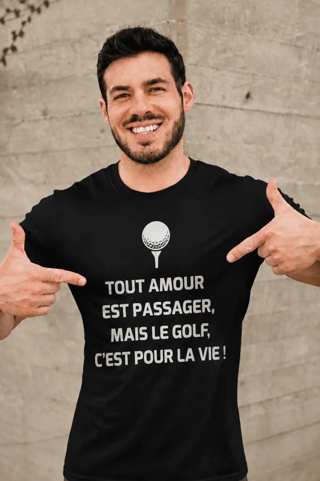 Homme souriant pointant son t-shirt noir imprimé « Tout amour est passager » en lettres blanches